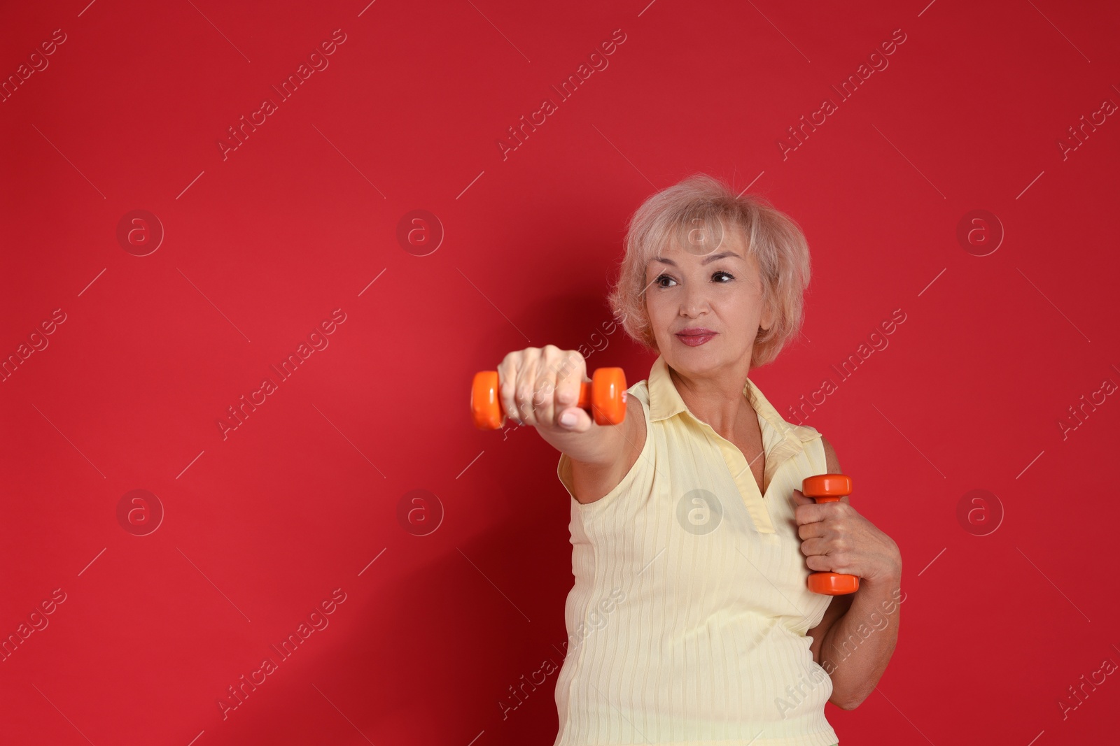 Photo of Senior woman exercising with dumbbells on red background, space for text