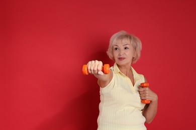 Photo of Senior woman exercising with dumbbells on red background, space for text