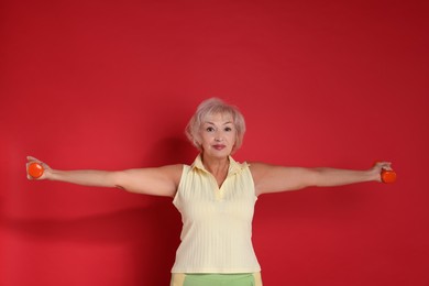 Photo of Senior woman exercising with dumbbells on red background