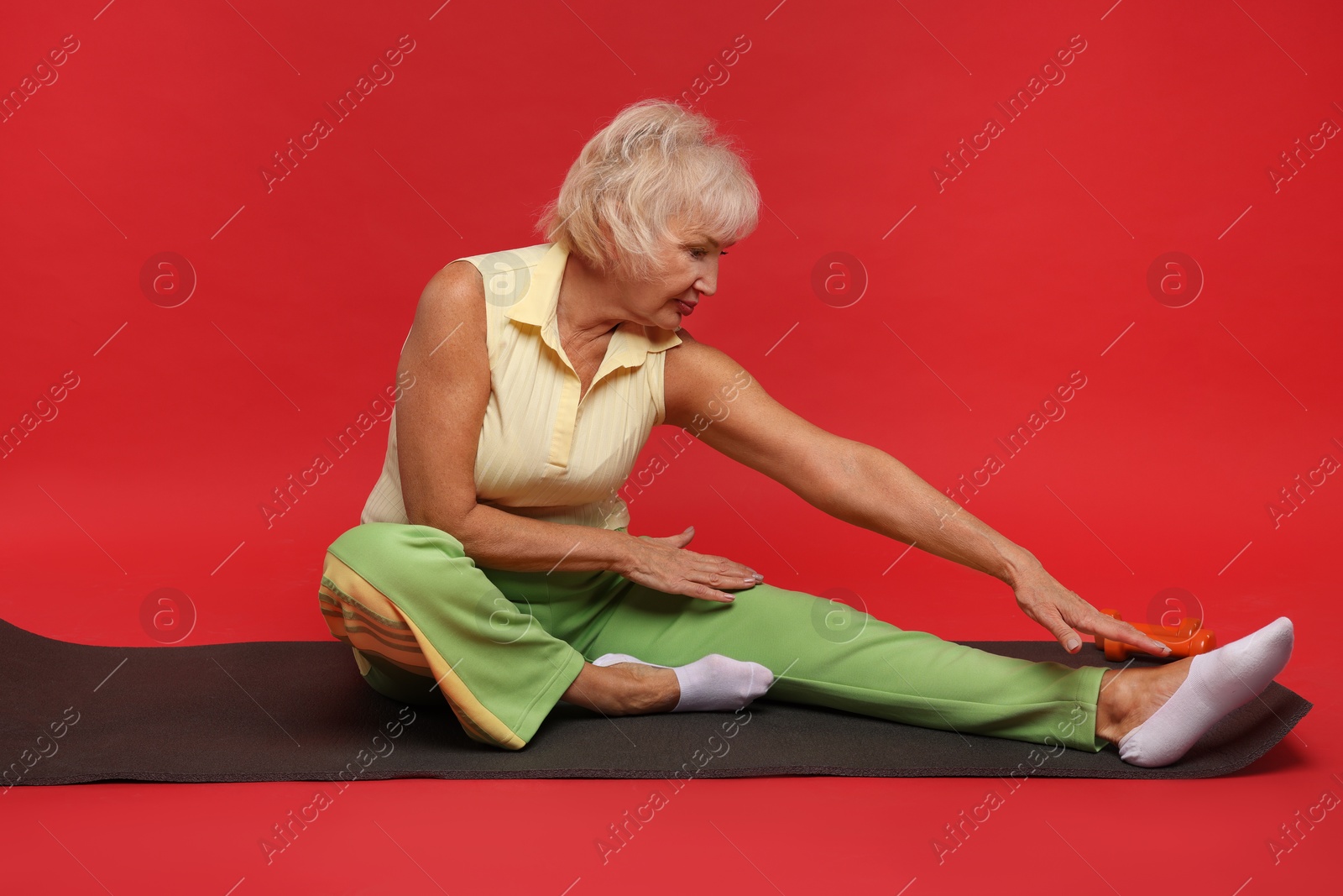 Photo of Senior woman exercising with fitness mat on red background