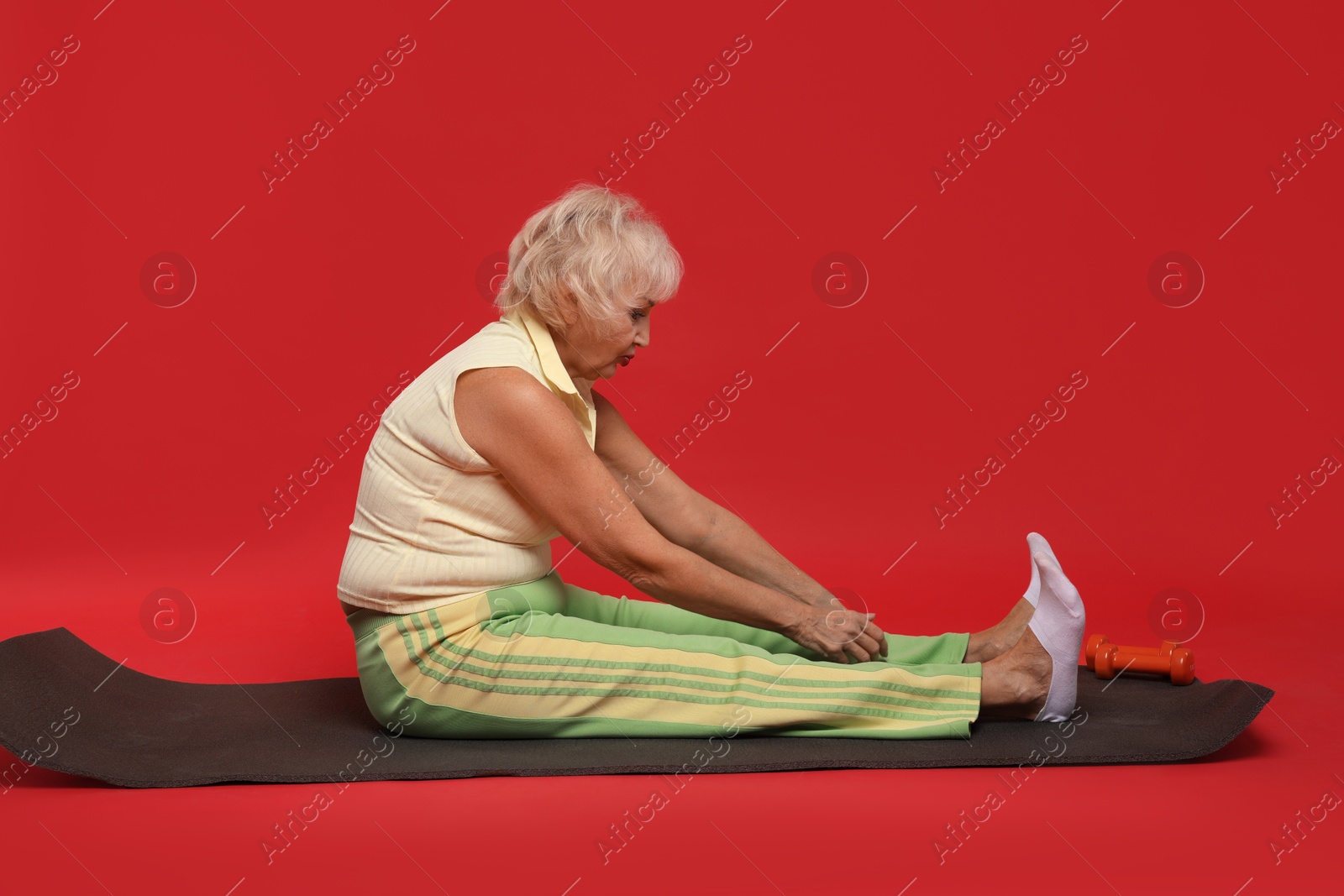 Photo of Senior woman exercising with fitness mat on red background