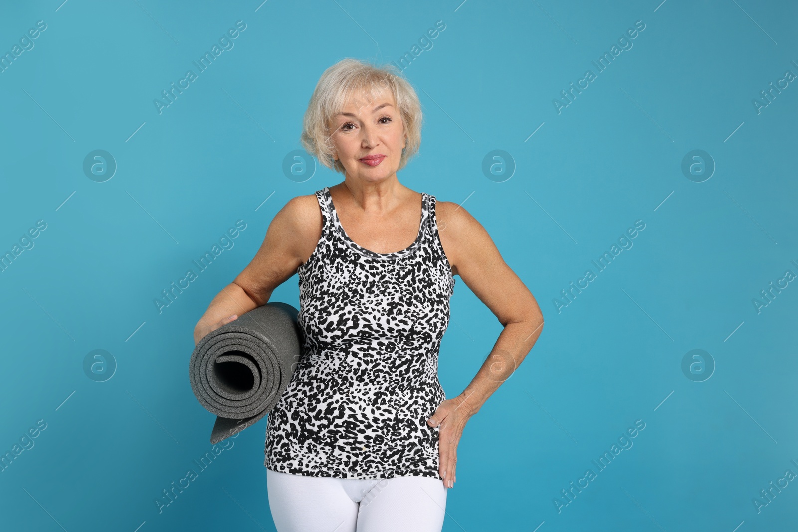 Photo of Senior woman with fitness mat on light blue background, space for text