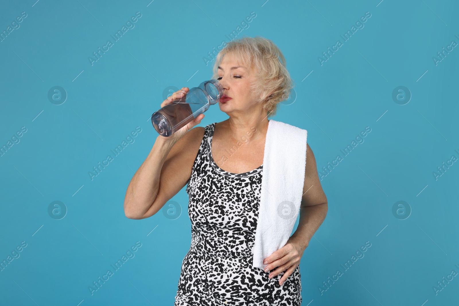 Photo of Senior woman with towel and water on light blue background