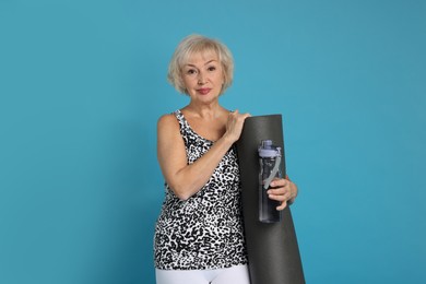 Photo of Senior woman with fitness mat and water on light blue background