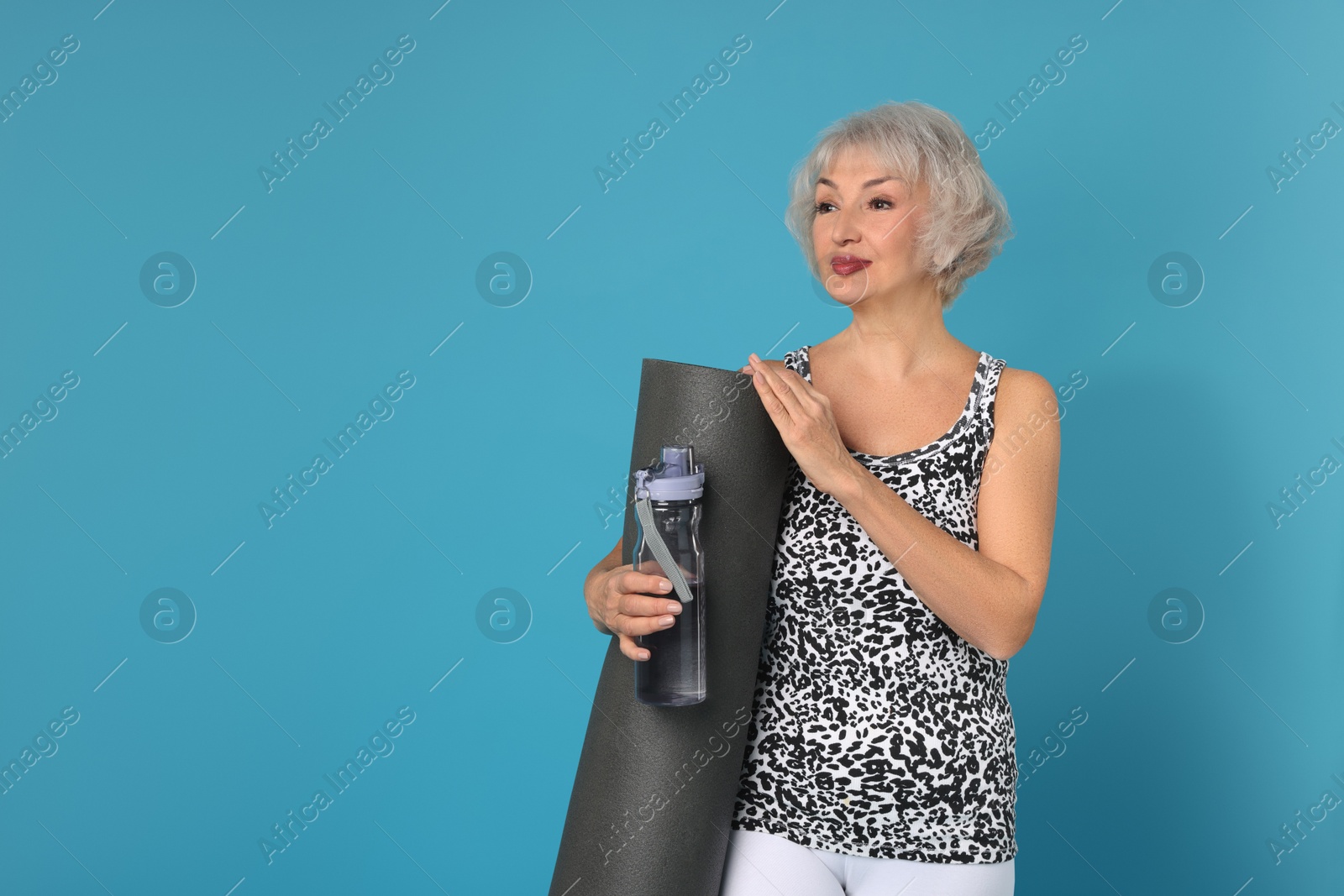 Photo of Senior woman with fitness mat and water on light blue background, space for text