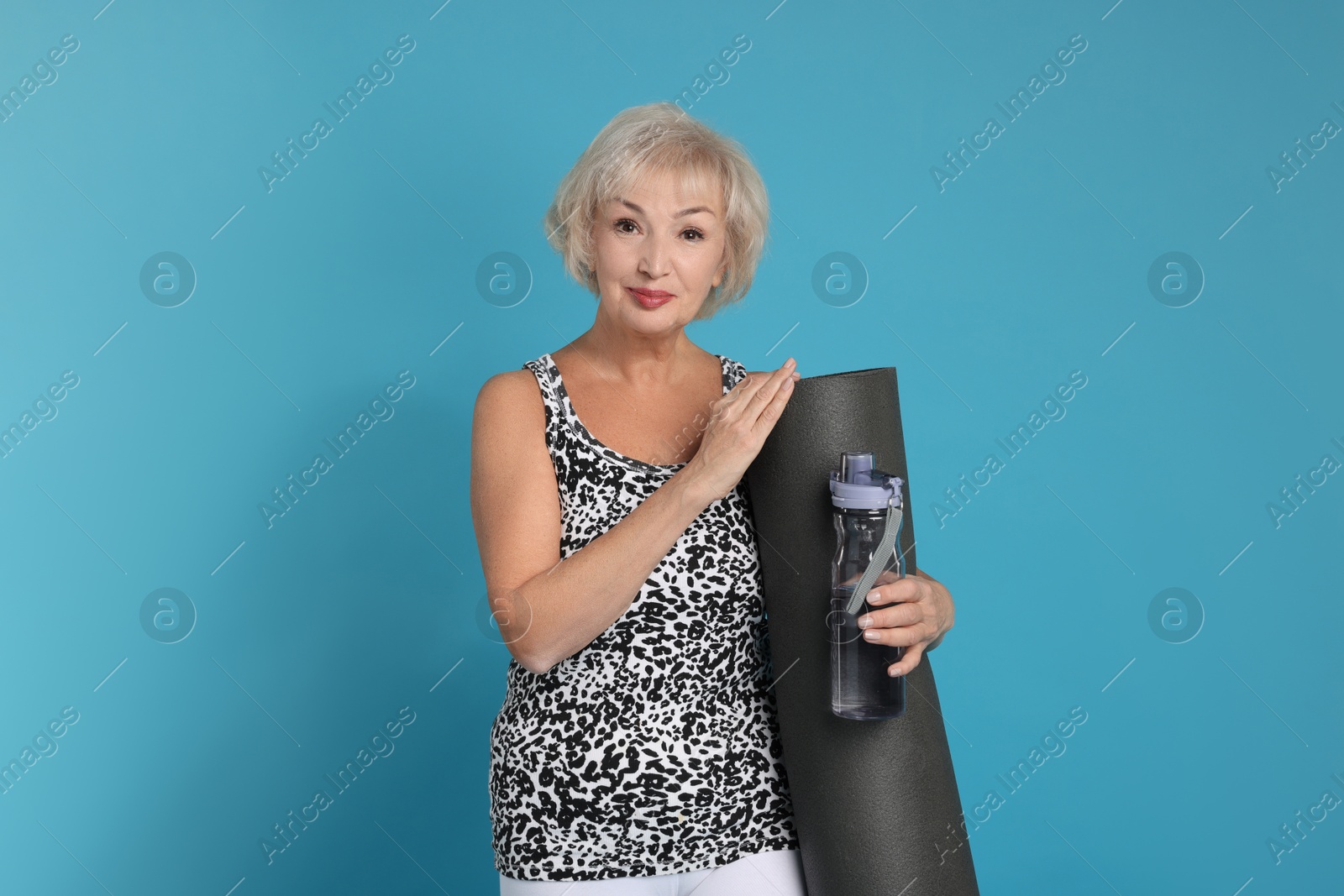 Photo of Senior woman with fitness mat and water on light blue background