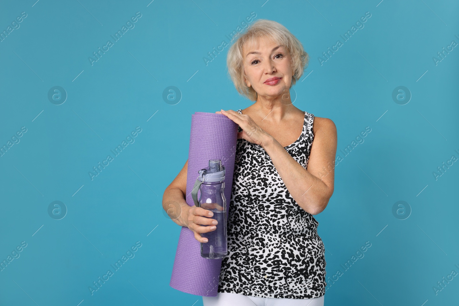 Photo of Senior woman with fitness mat and water on light blue background, space for text