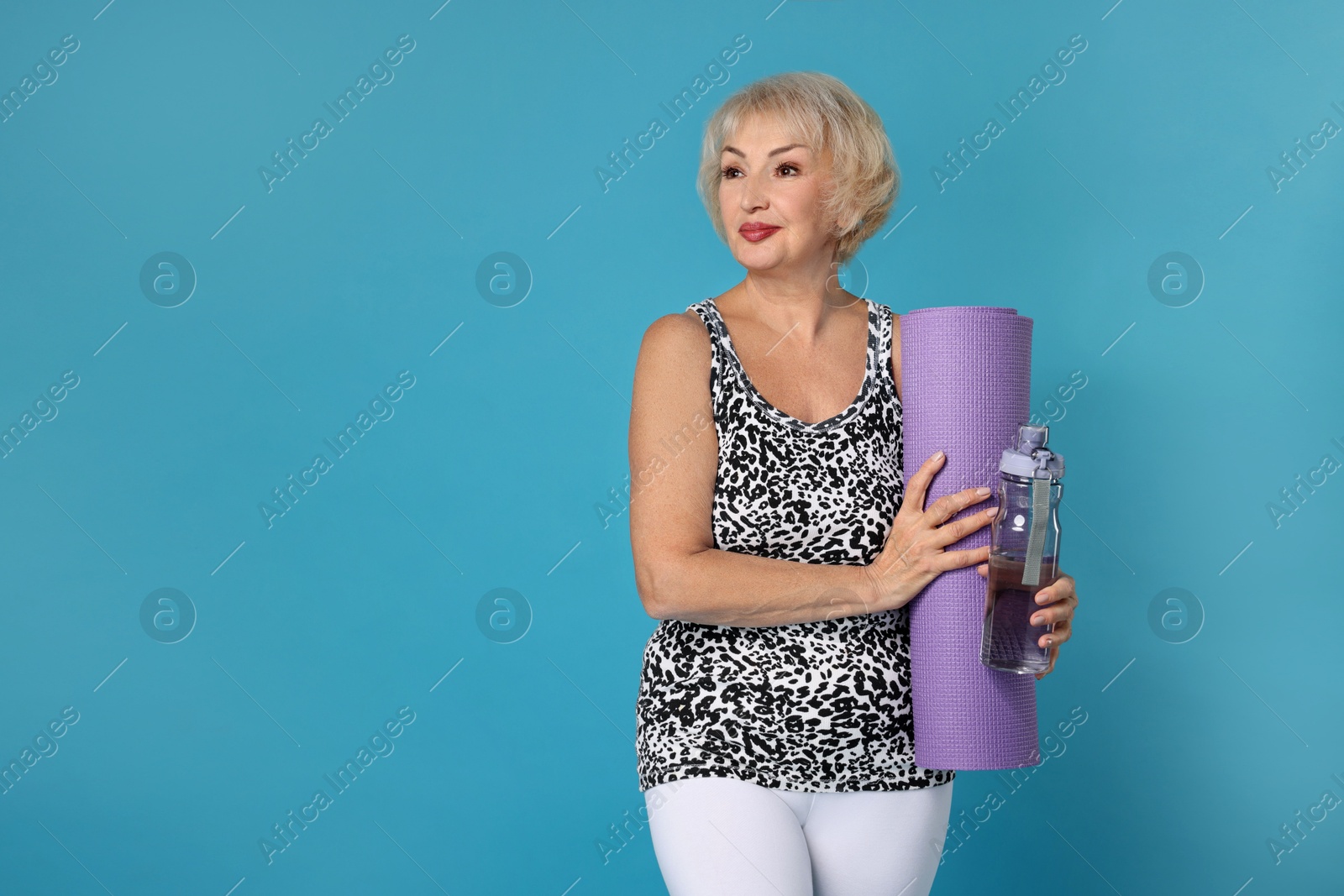 Photo of Senior woman with fitness mat and water on light blue background, space for text