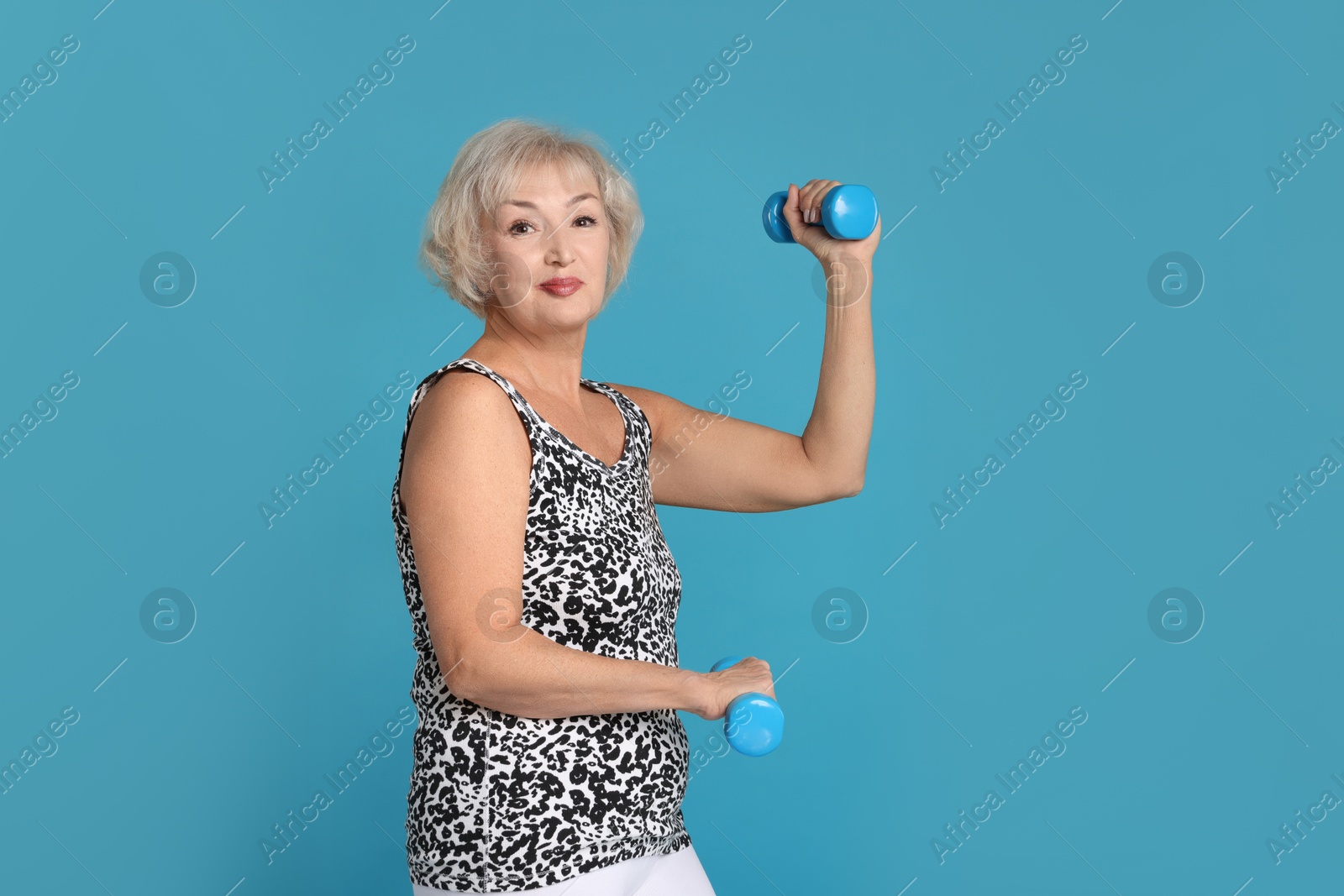 Photo of Senior woman exercising with dumbbells on light blue background. Space for text