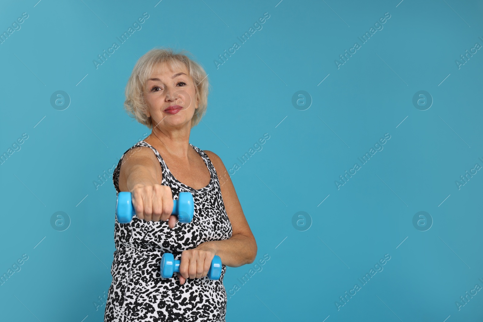 Photo of Senior woman exercising with dumbbells on light blue background, space for text