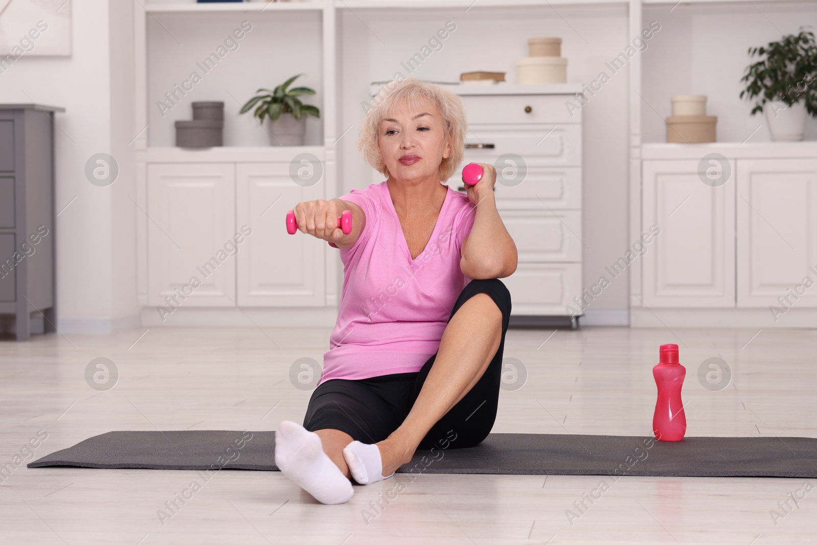 Photo of Senior woman exercising with fitness mat and dumbbells at home