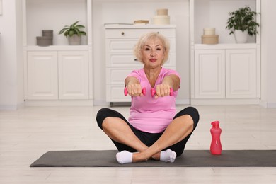 Photo of Senior woman exercising with fitness mat and dumbbells at home