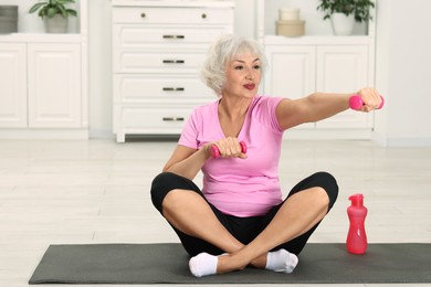 Photo of Senior woman exercising with fitness mat and dumbbells at home