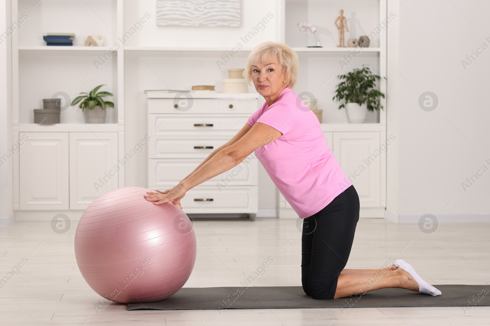 Photo of Senior woman exercising with fitness mat and ball at home