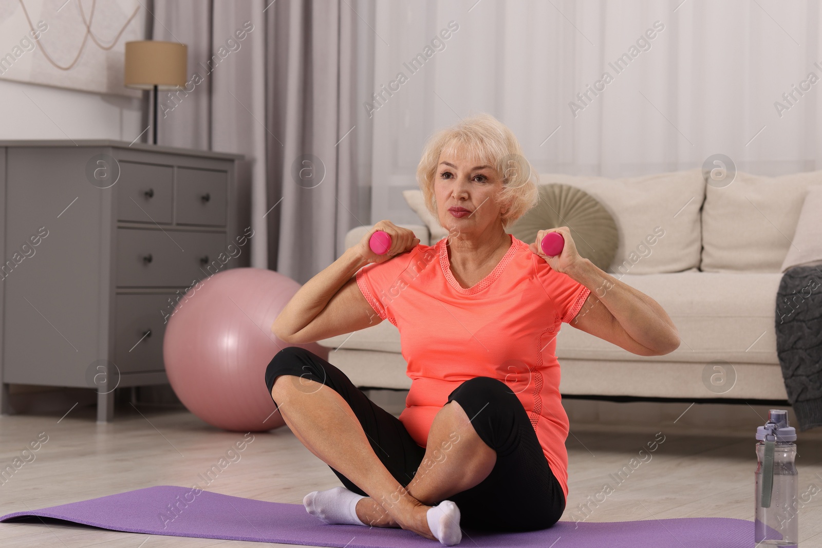 Photo of Senior woman exercising with fitness mat and dumbbells at home