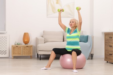 Photo of Senior woman exercising with fitness ball and dumbbells at home, space for text