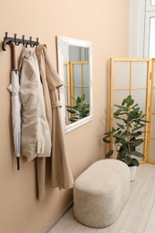 Photo of Coat rack with clothes, pouffe, houseplant and mirror in hallway. Interior design