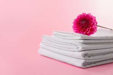 Photo of Stacked clean bed linens and flower on pink background, space for text