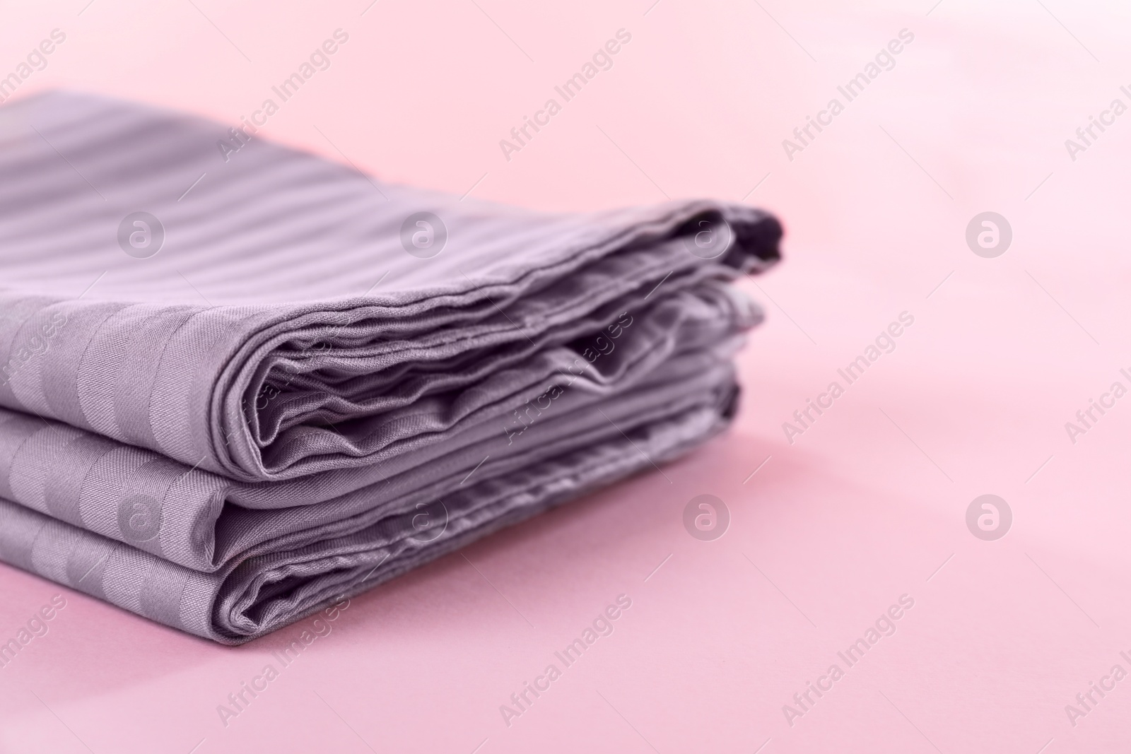 Photo of Stacked clean bed linens on pink background, closeup. Space for text