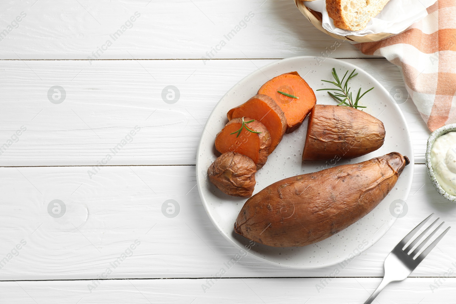 Photo of Tasty cooked sweet potatoes served with rosemary and sauce on white wooden table, top view. Space for text