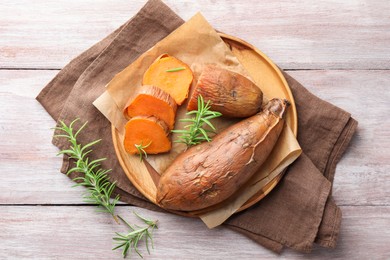 Photo of Tasty cooked sweet potatoes and rosemary on wooden table, top view