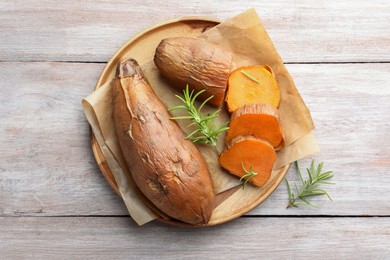 Photo of Tasty cooked sweet potatoes and rosemary on wooden table, top view