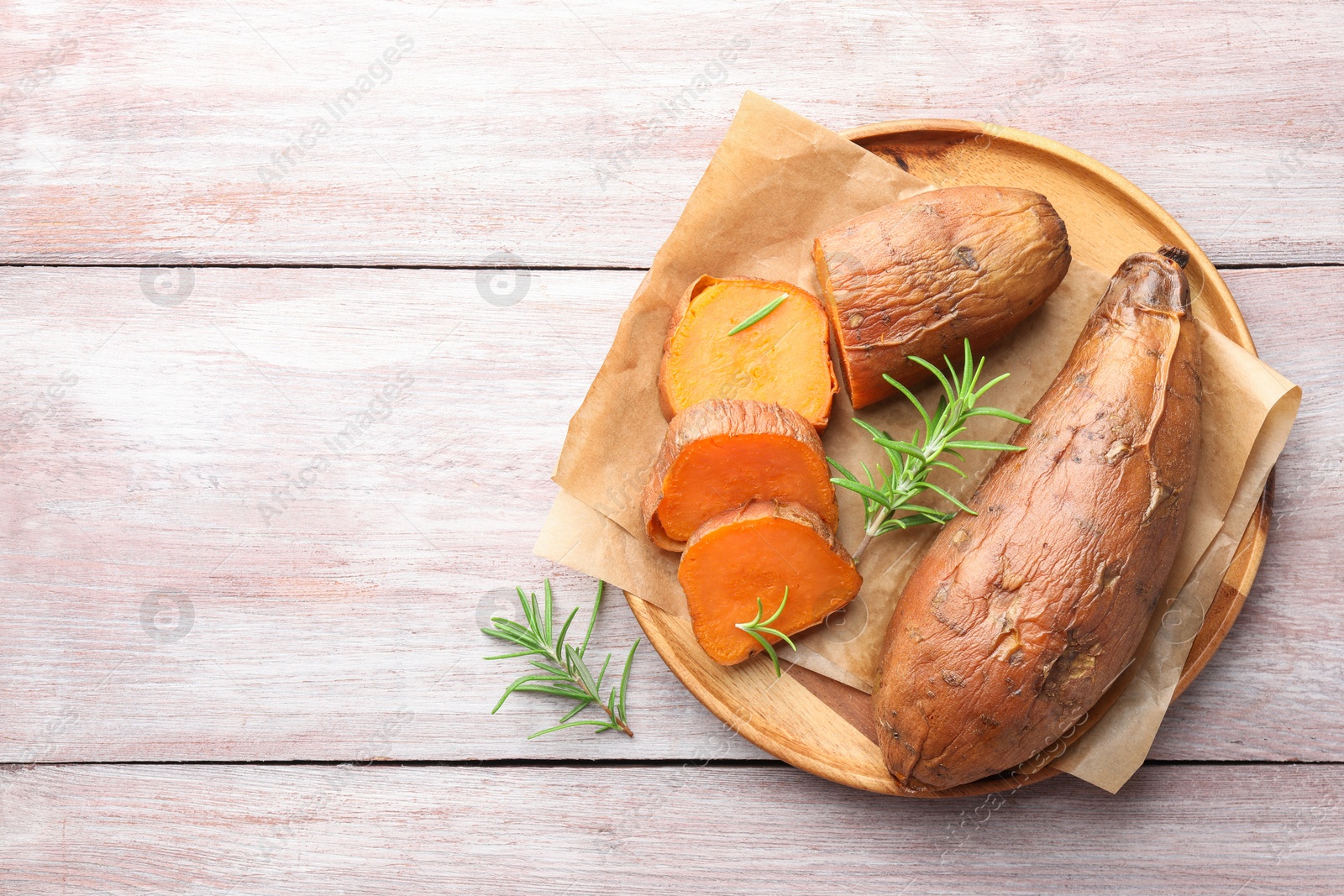 Photo of Tasty cooked sweet potatoes and rosemary on wooden table, top view. Space for text