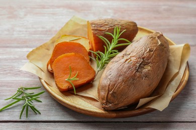 Photo of Tasty cooked sweet potatoes and rosemary on wooden table, closeup