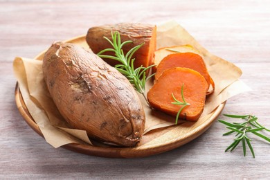 Photo of Tasty cooked sweet potatoes and rosemary on wooden table, closeup