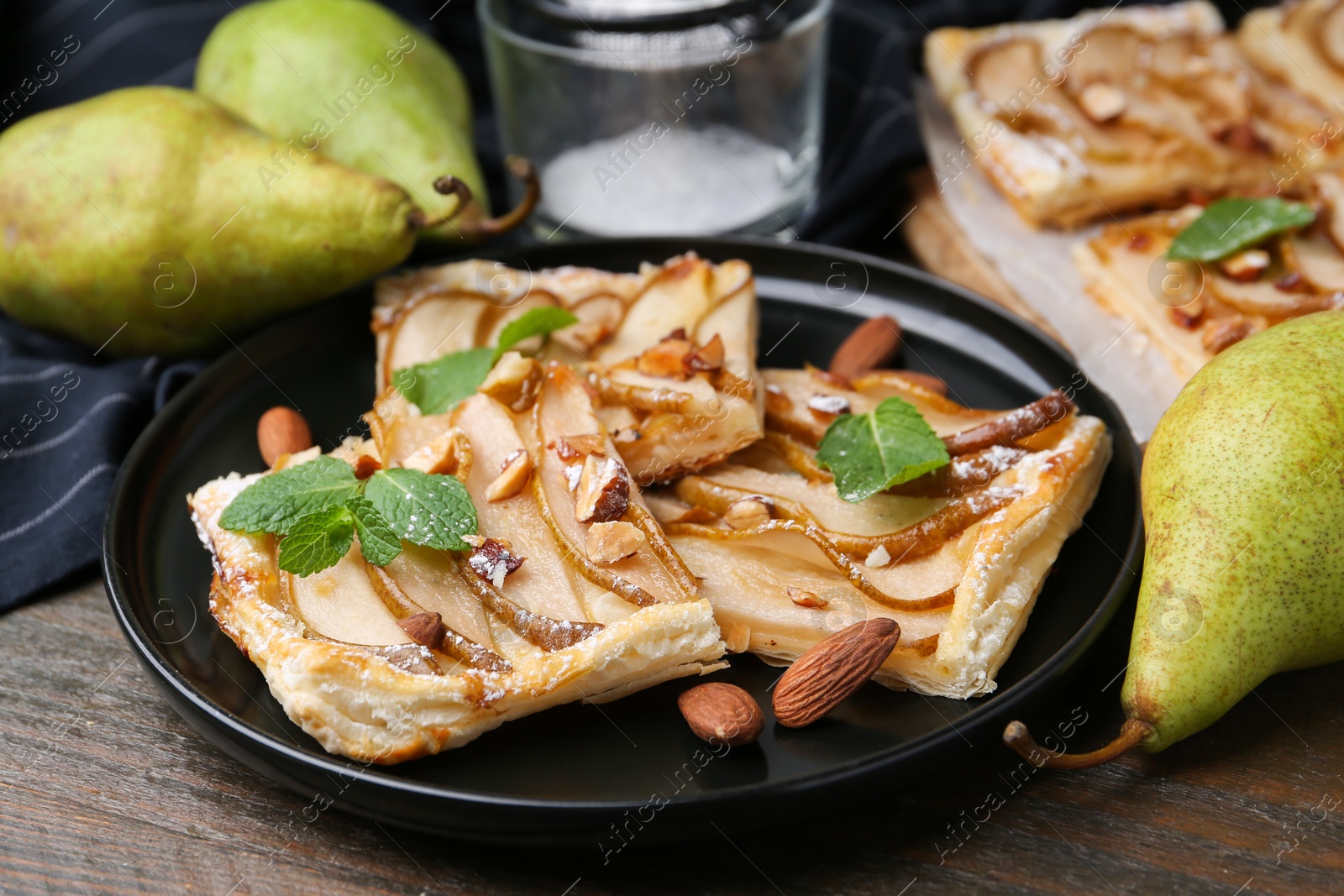 Photo of Pieces of tasty puff pastry pie with pears, mint and almonds on wooden table, closeup