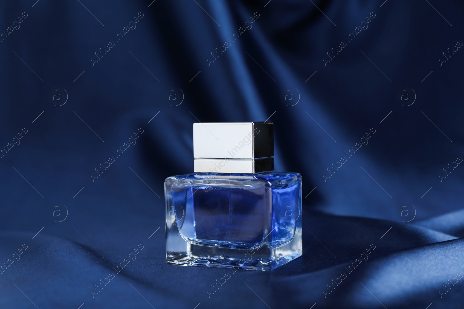 Photo of Bottle of perfume and dark blue silk fabric