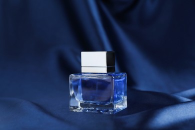 Photo of Bottle of perfume and dark blue silk fabric