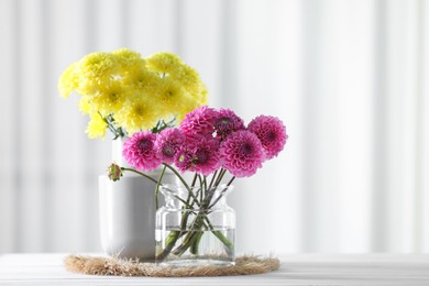 Photo of Beautiful yellow and pink flowers in vases on white wooden table at home