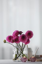 Photo of Beautiful pink flowers in vase and burning candles on wooden table at home. Space for text