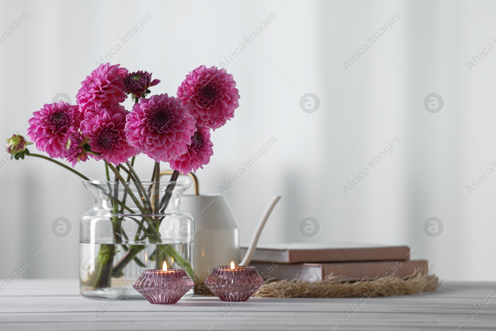 Beautiful pink flowers in vase, books and burning candles on wooden table at home. Space for text Photo of Beautiful pink flowers in vase, books and burning candles on wooden table at home. Space for text