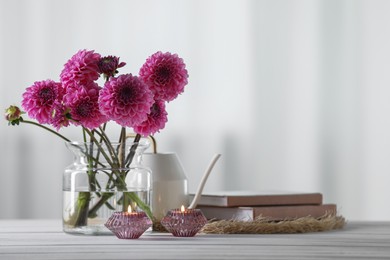 Photo of Beautiful pink flowers in vase, books and burning candles on wooden table at home. Space for text