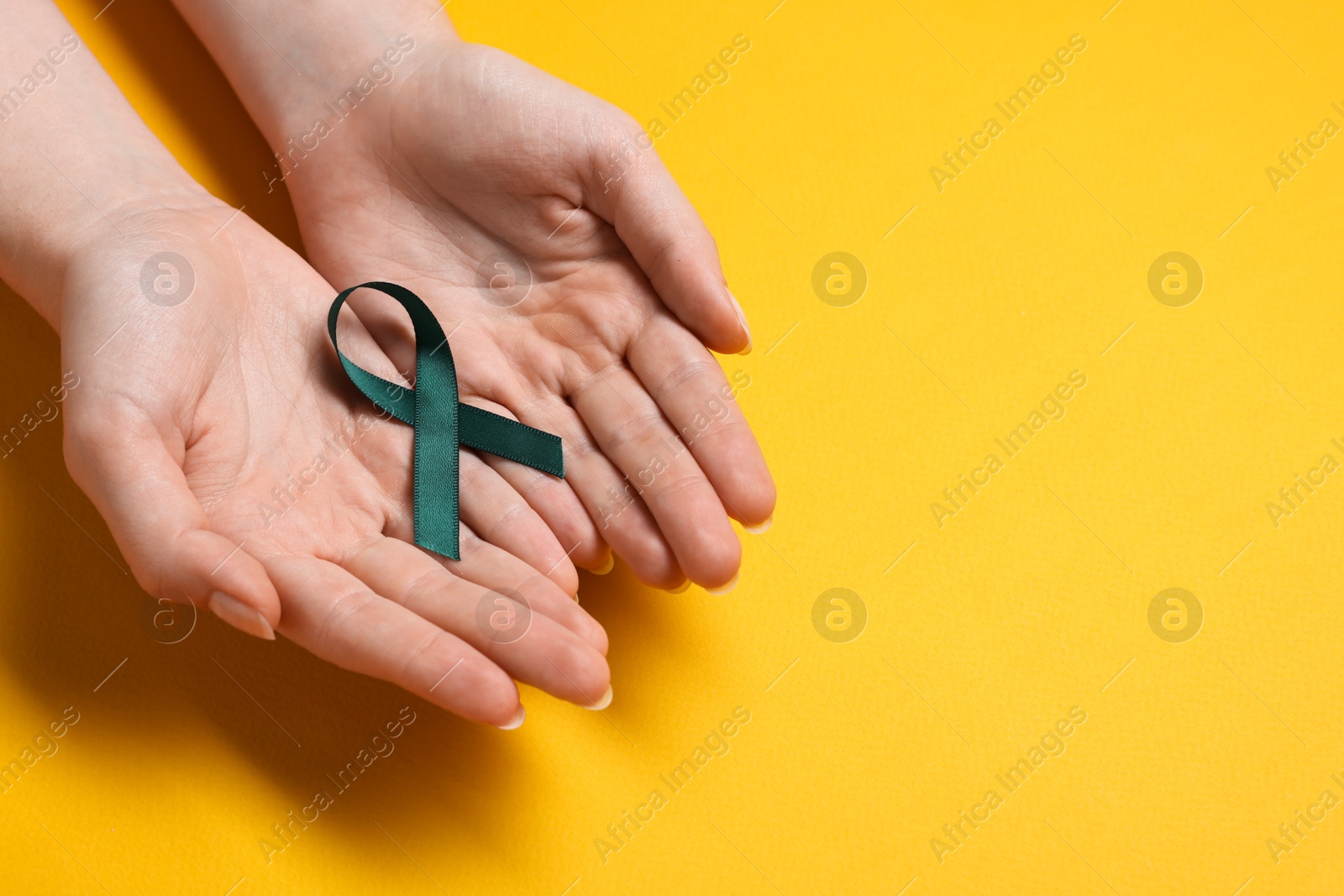 Photo of Woman with teal ribbon on yellow background, top view with space for text. Ovarian cancer and gynecological disorders awareness