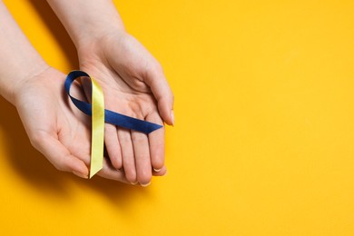 Photo of Woman with colorful ribbon on yellow background, top view and space for text. Down syndrome awareness