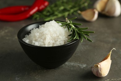 Photo of Sea salt in bowl, rosemary and garlic on grey table, closeup