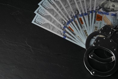 Photo of Corruption. Dollar banknotes and handcuffs on black table, top view. Space for text