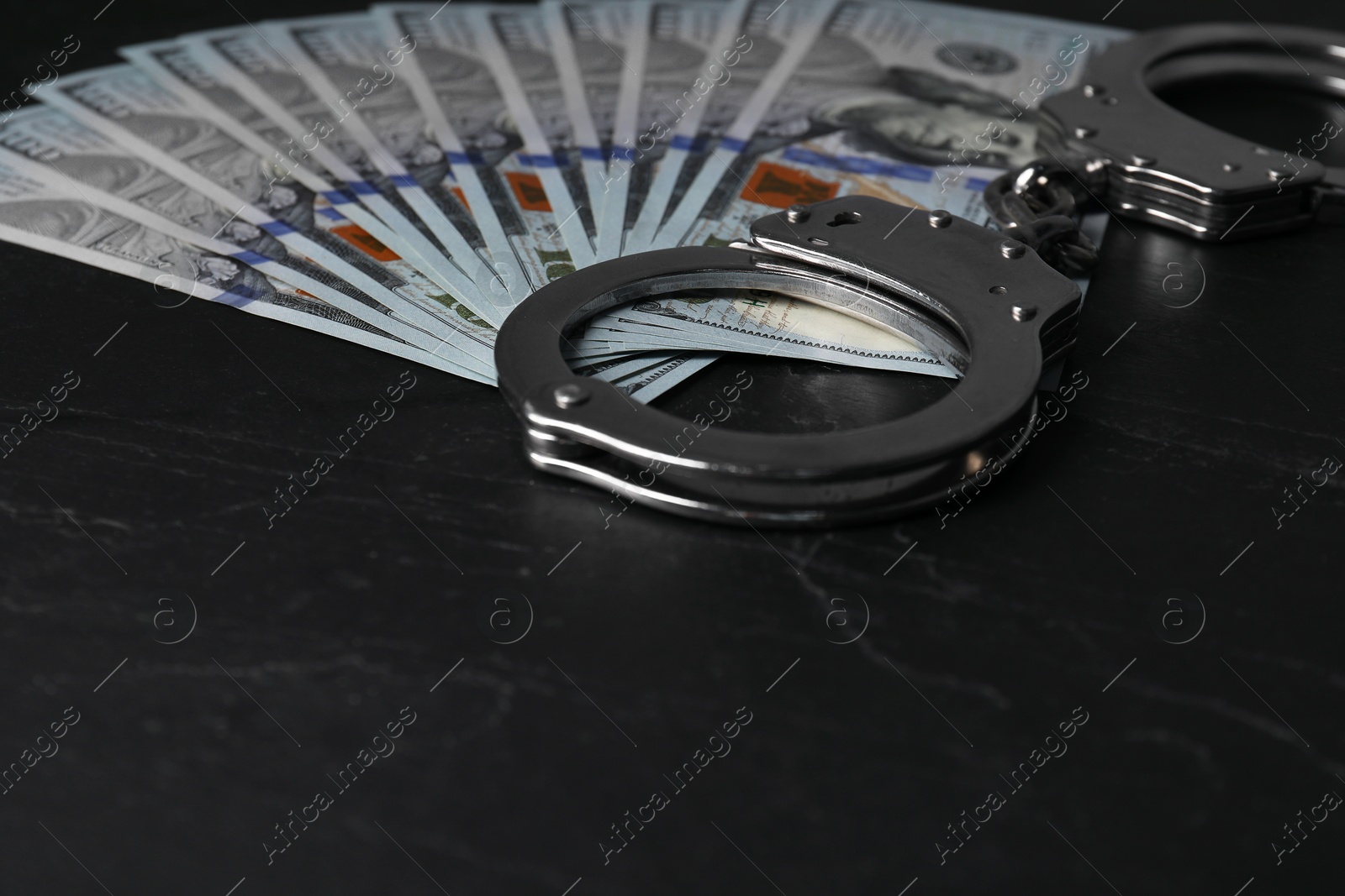 Photo of Corruption. Dollar banknotes and handcuffs on black table, closeup