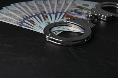 Photo of Corruption. Dollar banknotes and handcuffs on black table, closeup