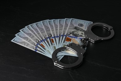 Photo of Corruption. Dollar banknotes and handcuffs on black table