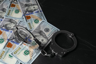 Photo of Corruption. Handcuffs and dollar banknotes on black table, closeup