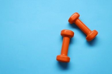 Photo of Two dumbbells on light blue background, top view. Space for text