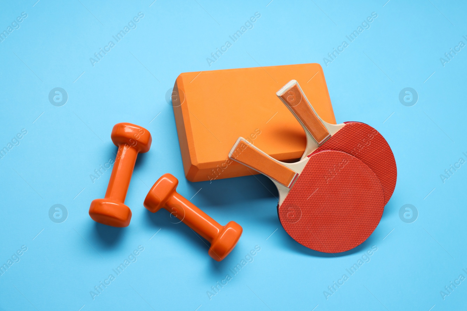 Photo of Dumbbells, yoga block and ping pong rackets on light blue background, flat lay