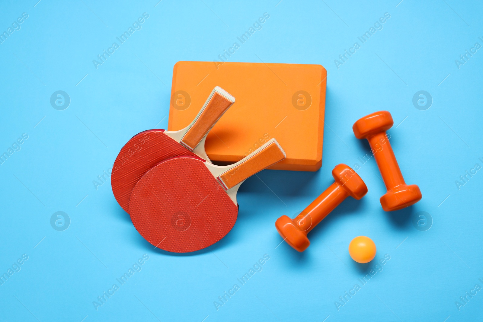 Photo of Dumbbells, yoga block, ping pong rackets and ball on light blue background, flat lay