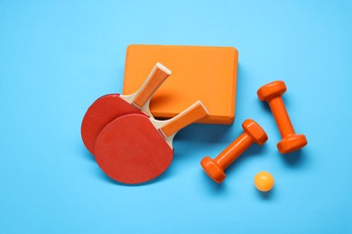 Dumbbells, yoga block, ping pong rackets and ball on light blue background, flat lay