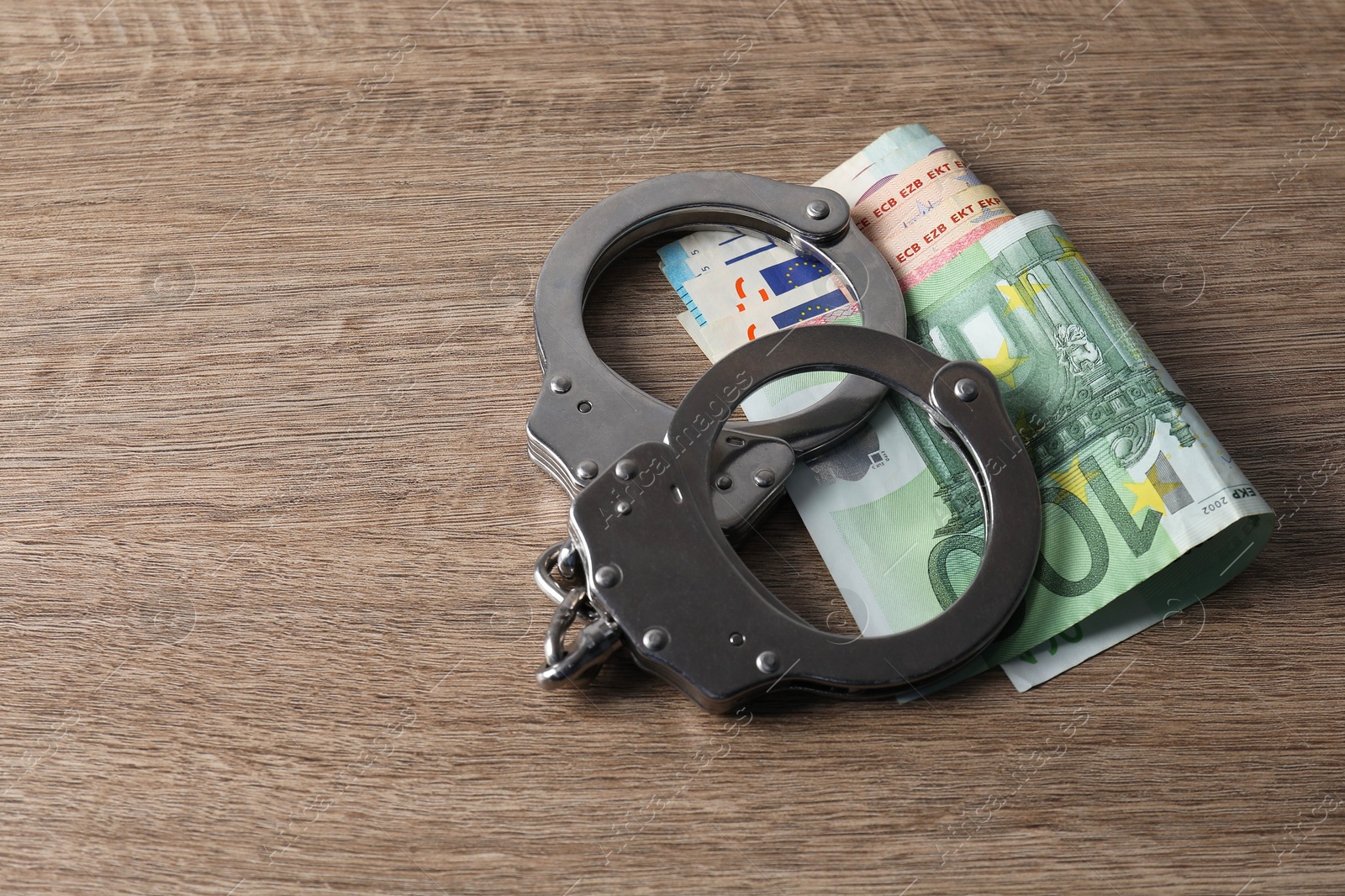 Photo of Corruption. Handcuffs and euro banknotes on wooden table