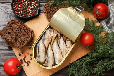 Photo of Tasty sprats in tin can served on wooden table, flat lay